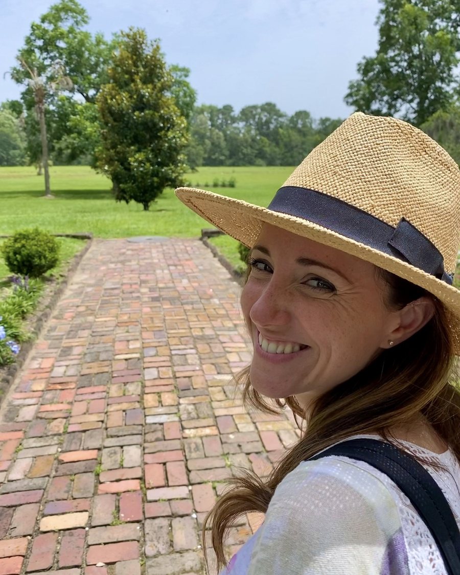 Sydney, founder of Girasole Wellness, smiling outdoors on a brick garden path